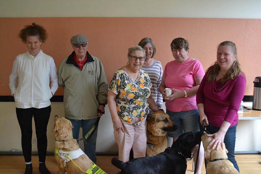 Six people stand together, accompanied by four happy service dogs.