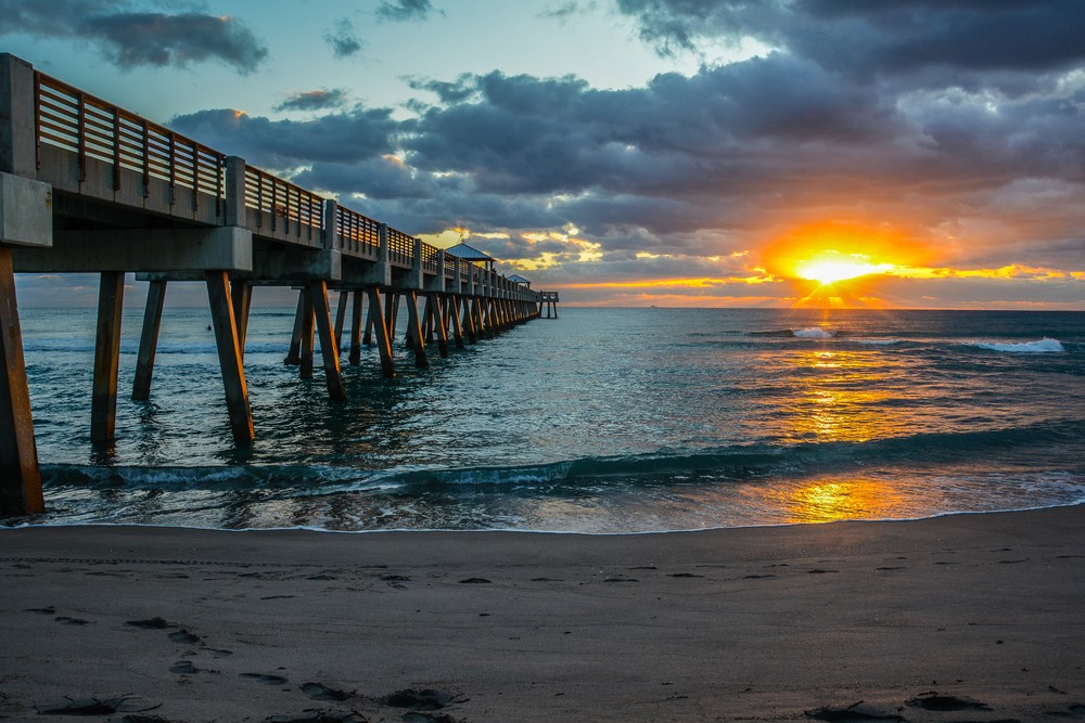 The sun as it rises above clouds by a fishing pier