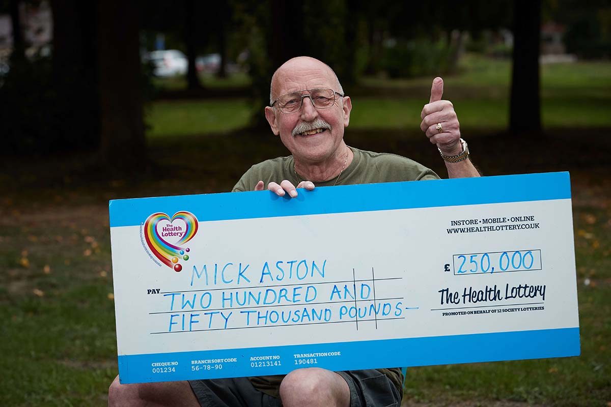 Mick holds up a Health Lottery giant check for £250,000